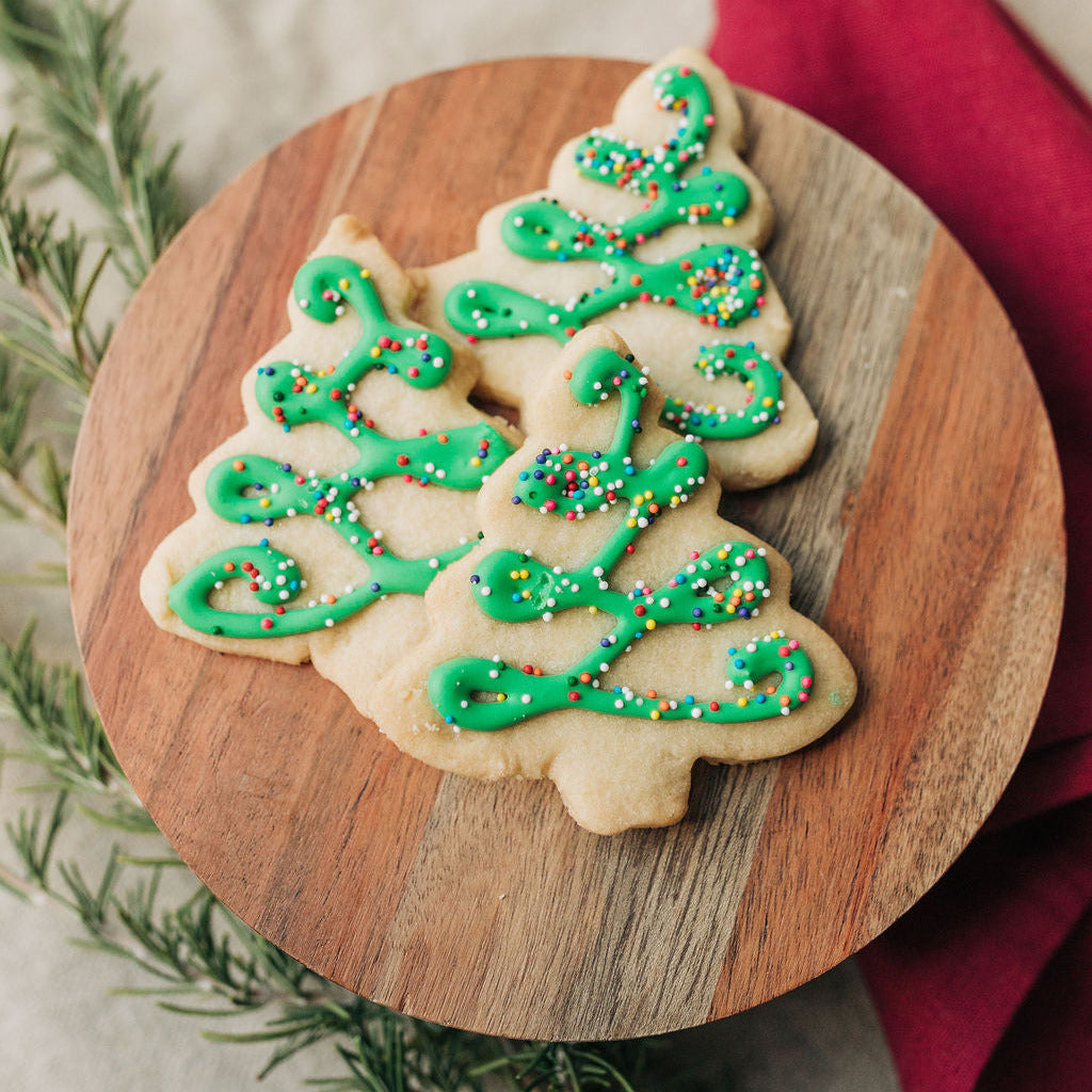 Christmas tree-shaped cookies with green icing and sprinkles on a wooden board.