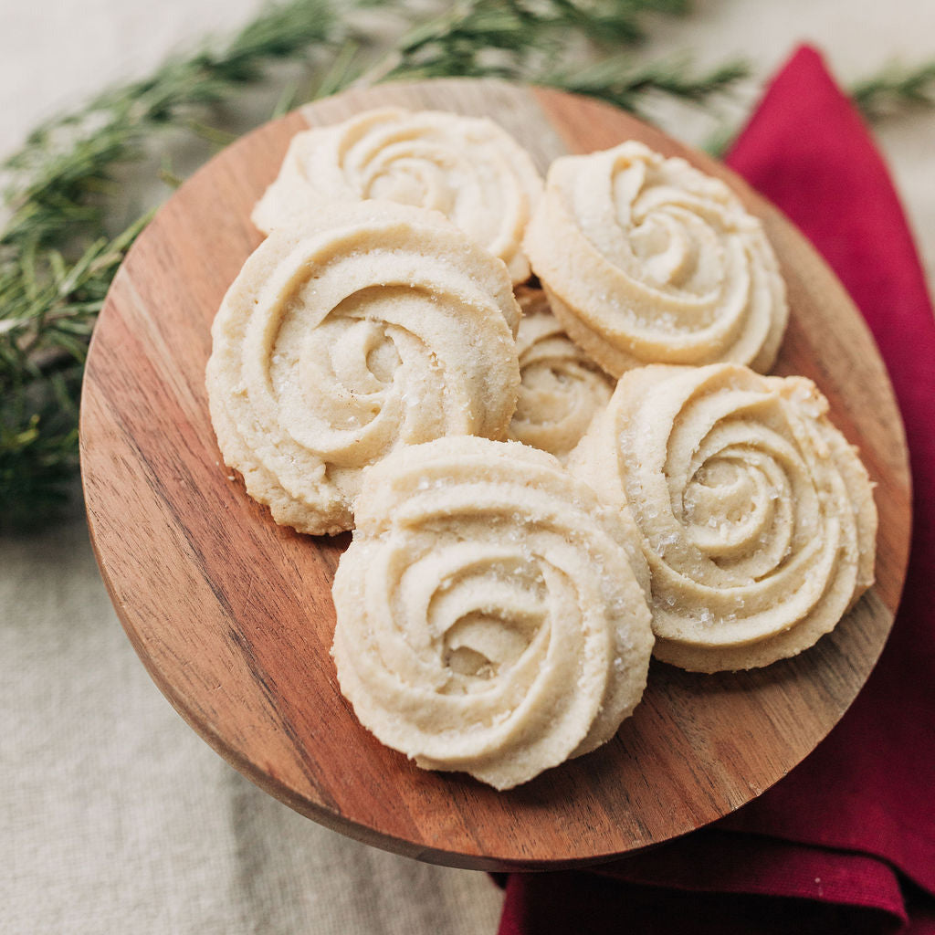 Decorative cookies on a wooden plate with a red napkin and greenery in the background