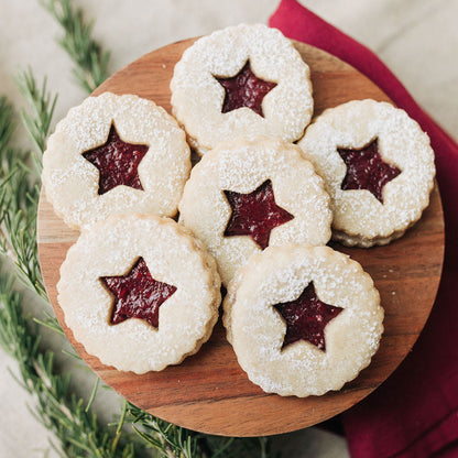 Decorative cookies with red star-shaped centers on a wooden board, surrounded by greenery and a red cloth.